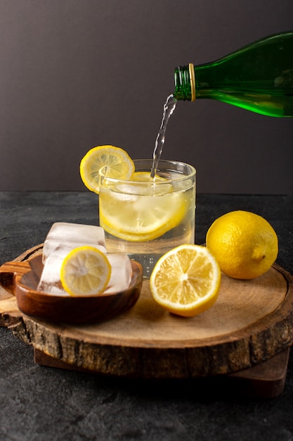 Een vooraanzicht water met verse frisse citroen drankje in glas gieten met ijsblokjes met gesneden citroenen op dark