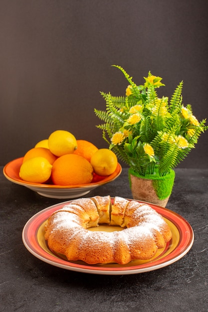 Een vooraanzicht zoete ronde cake met suikerpoeder gesneden zoete heerlijke geïsoleerde cake binnen plaat samen met citroenen en grijze achtergrond biscuit suiker koekje