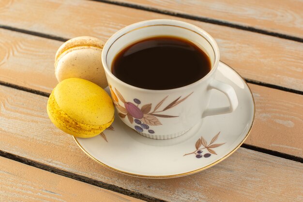 Gratis foto een vooraanzichtkop van hete en sterke koffie met franse macarons op het roomkleurige rustieke bureau drinkt sterke koffiefoto