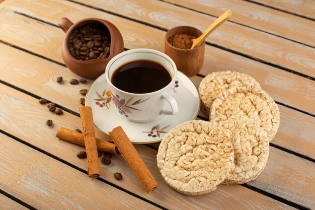 Een vooraanzichtkop van hete en sterke koffie met verse bruine koffiezaden en crackers op de korrel van de de koffiezaaddrank van het room rustieke bureau