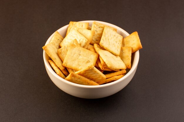 Een voorzijde sloot omhoog de gezouten kaas van chips smakelijke crackers binnen witte plaat op het donkere achtergrondsnack zoute scherpe voedsel