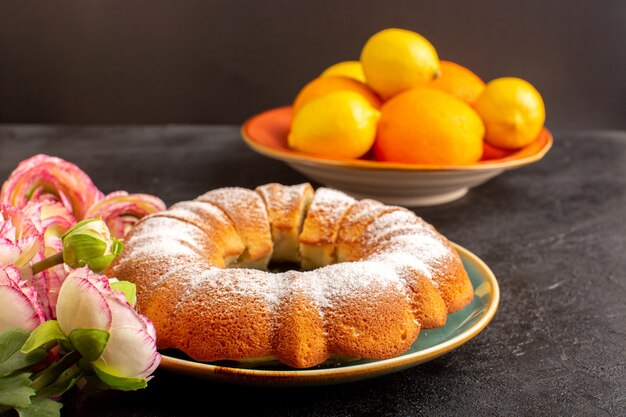 Een voorzijde sloot omhoog zoete ronde cake met suikerpoeder bovenop samen met citroenen gesneden zoete heerlijke geïsoleerde binnenplaat