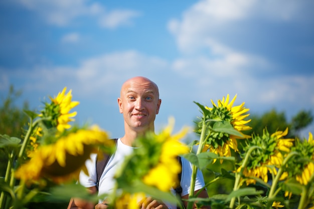 Een vrolijke kale man in een veld met bloeiende gele zonnebloemen tegen een blauwe hemel staat lachend