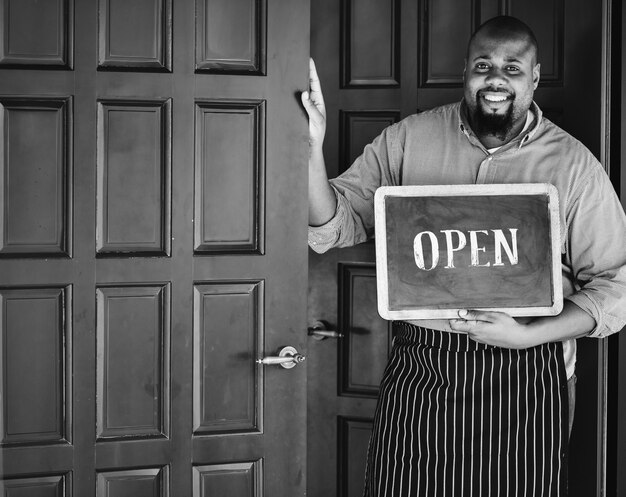 Een vrolijke kleine bedrijfseigenaar met open teken