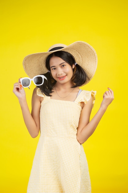 Een vrolijke mooie vrouw die een grote hoed met witte bril op een geel draagt.