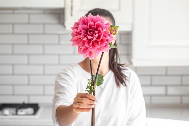 Gratis foto een vrouw bedekt haar gezicht met een roze dahlia bloem op een witte binnengrond