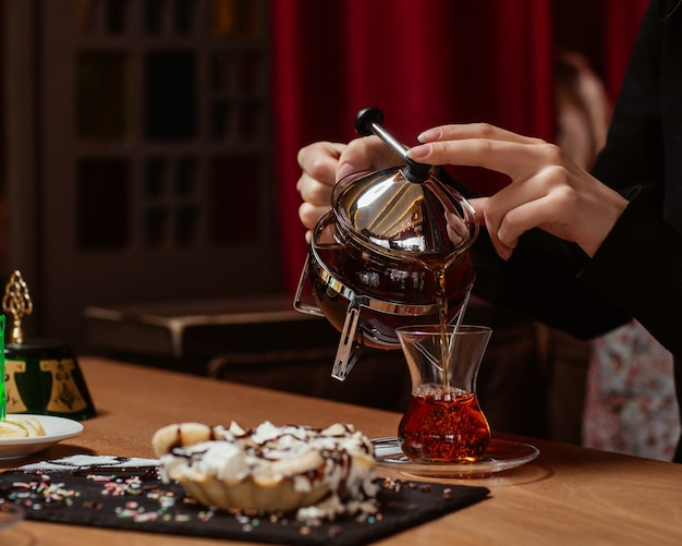 Een vrouw die een glas thee op de theetafel met snoep zet