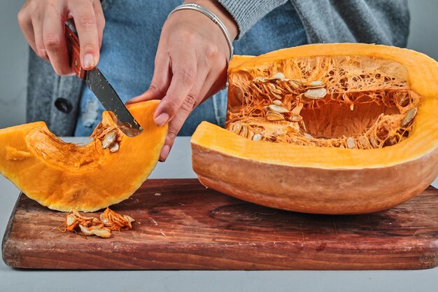 Een vrouw die met de hand een plakje pumpkon snijdt met mes op een houten bord.