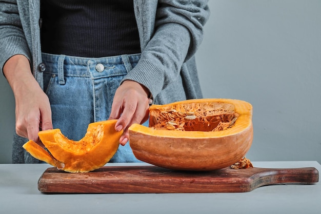 Een vrouw die met de hand een plakje pumpkon snijdt met mes op een houten bord.