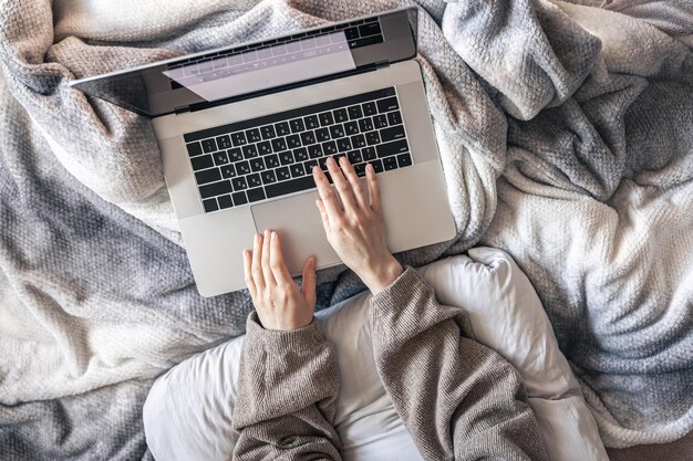 Een vrouw die op een laptop werkt terwijl ze in bed ligt bovenaanzicht