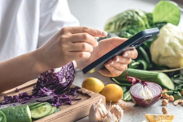 Een vrouw gebruikt een smartphone in de keuken terwijl ze een groente salade bereidt