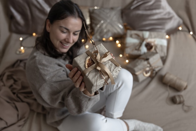 Een vrouw houdt een kerstgeschenkdoos vast die is versierd in ambachtelijke stijl, versierd met gedroogde bloemen en een droge sinaasappel, verpakt in ambachtelijk papier.