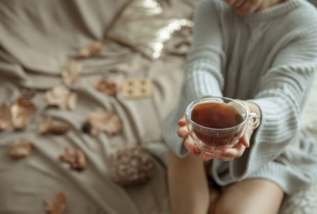Een vrouw in een gezellige gebreide trui houdt een kopje thee in haar handen, kopieer ruimte.