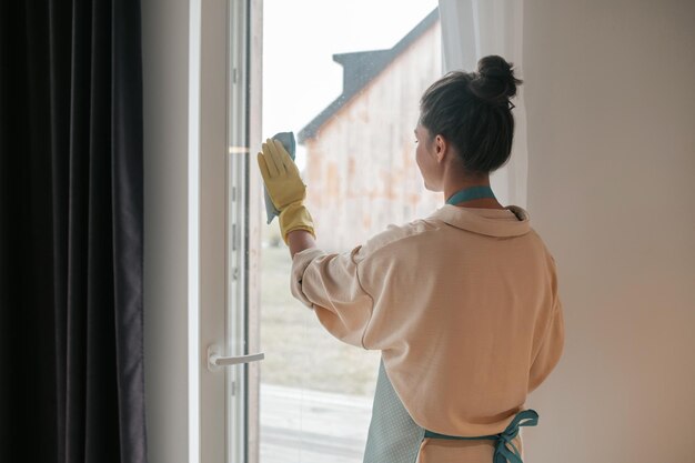 Een vrouw in schort die de ramen schoonmaakt en er betrokken uitziet