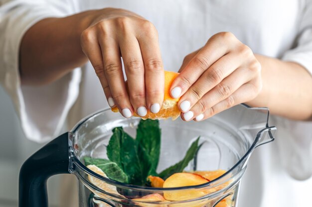 Een vrouw knijpt sinaasappelsap in een blender om een fruit smoothie te maken