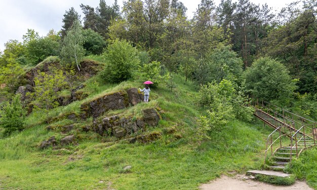 Een vrouw loopt onder een paraplu in de bergen, tussen de rotsen bedekt met groen