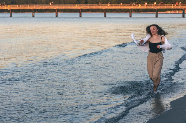 Een vrouw loopt op blote voeten langs de zee bij zonsondergang kopieerruimte
