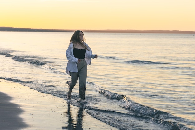 Een vrouw loopt op blote voeten langs de zee bij zonsondergang kopieerruimte