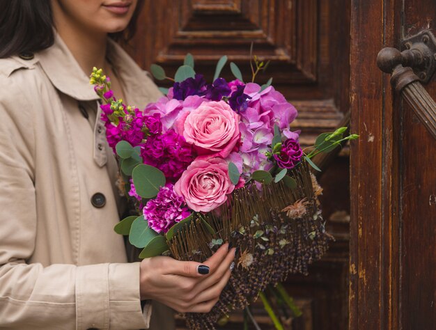 Een vrouw met een boeket van roze, paarse, paarse pioenrozen en rozen in de hand