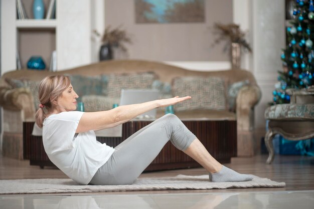 Een vrouw ouder dan 50 jaar die thuis yoga doet. Liggend op de vloer voert ze Asana-oefeningen uit. Een vrouw houdt van yoga.