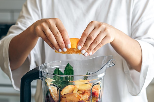 Gratis foto een vrouw perst sinaasappelsap in een blender en maakt een fruitsmoothie