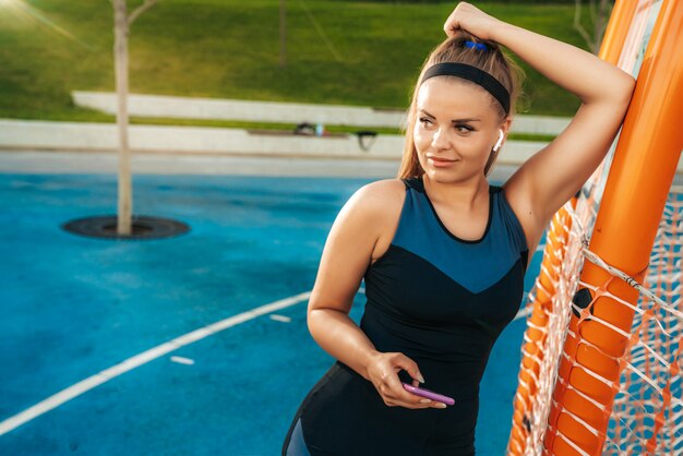 Een vrouw staat op de sportschool buiten met een telefoon