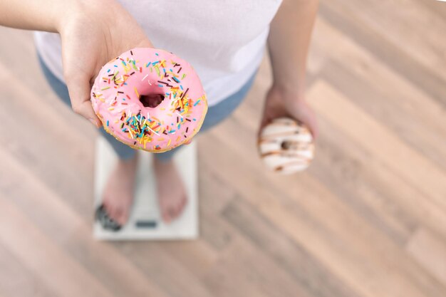 Een vrouw staat op de weegschaal en houdt donuts in haar handen bovenaanzicht kopieerruimte