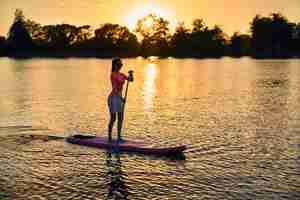 Gratis foto een vrouw staat op een paddleboard met een peddel.