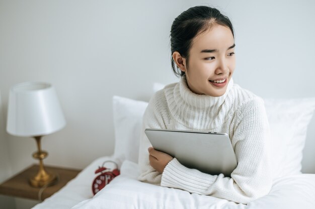 Een vrouw zittend op het bed, de laptop knuffelen en glimlachen.