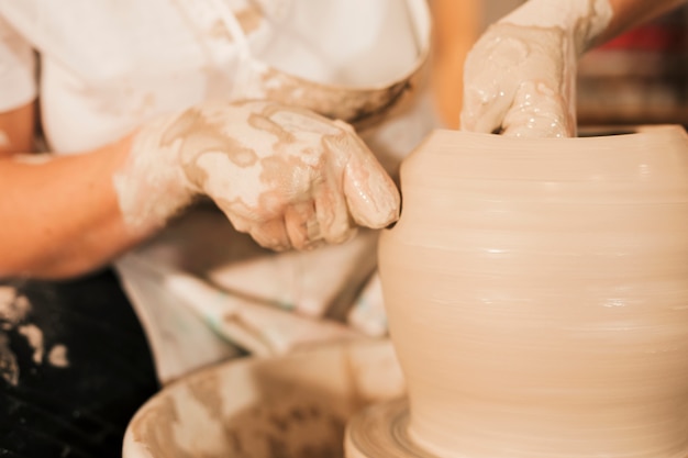 Gratis foto een vrouwelijke pottenbakker werkt aan het maken van een aarden pot aan het pottenbakkerswiel