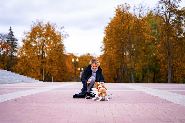 Een vrouwtje loopt in het park met een cavalier king charles spaniel. een vrouw die met een hond in het herfstpark loopt. cavalier king charles spaniël