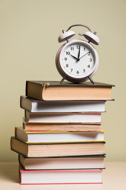 Een wekker bovenop gestapelde boeken over houten bureau