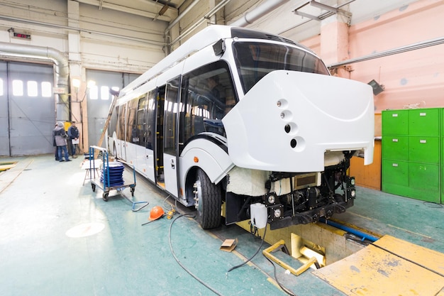 Een werkdag van moderne automatische busproductie met onafgewerkte auto's werknemers in beschermende uniforme autoproductie