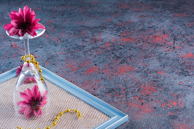 Een wijnglas met roze bloemen en gele ketting op frame.