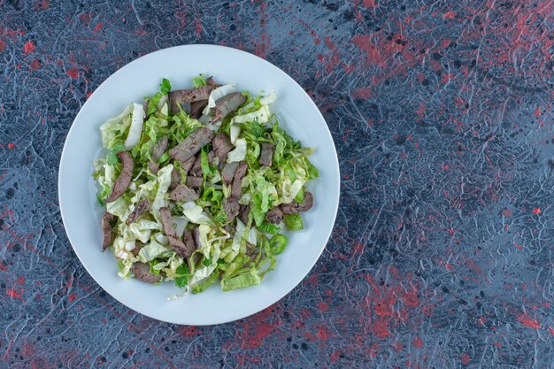 Een wit bord vlees met groentesalade.