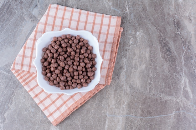 Een witte kom vol heerlijke chocolade maisballen op tafelkleed.