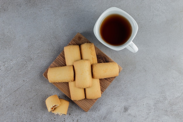 Een witte kop thee met zoete verse koekjes in een houten bord op een steen.