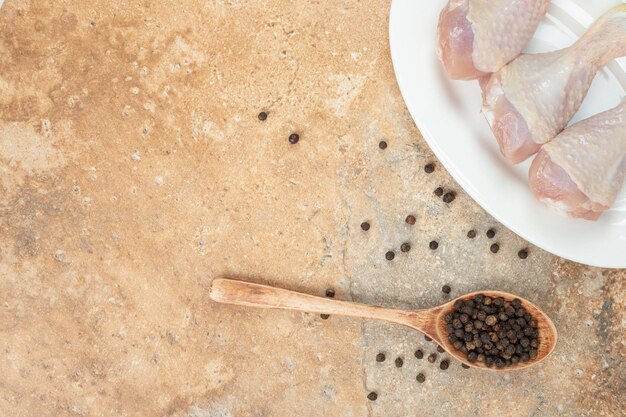 Een witte plaat met ongekookt kippenbeen met houten lepel peper