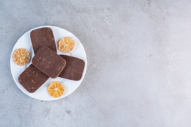 Een witte plaat van chocoladekoekjes met gesneden gedroogde citroen op grijze achtergrond.