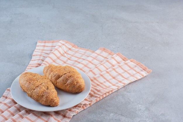 Een witte plaat van heerlijke zoete croissants op gestreept tafelkleed.