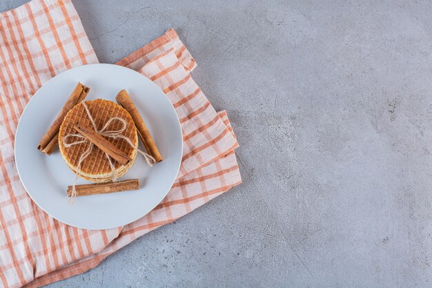 Een witte plaat van zoete wafels in touw met kaneelstokjes op een stenen oppervlak