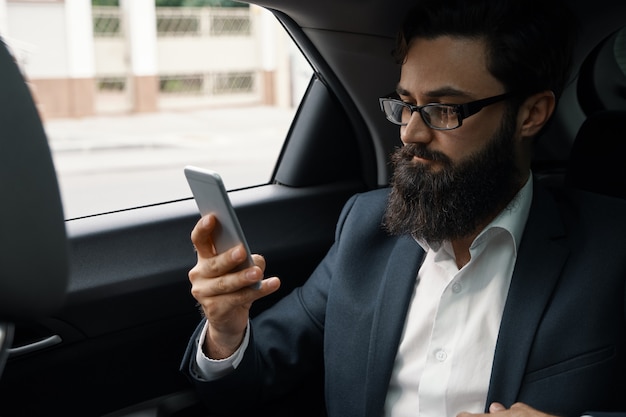 Een zakenman tijdens het reizen met de auto op de achterbank met behulp van een smartphone