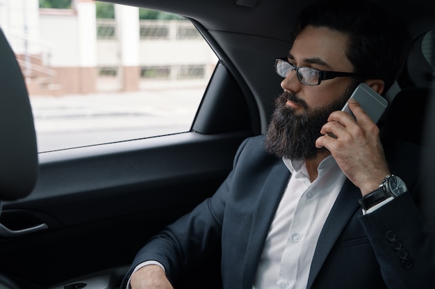 Een zakenman tijdens het reizen met de auto op de achterbank met behulp van een smartphone