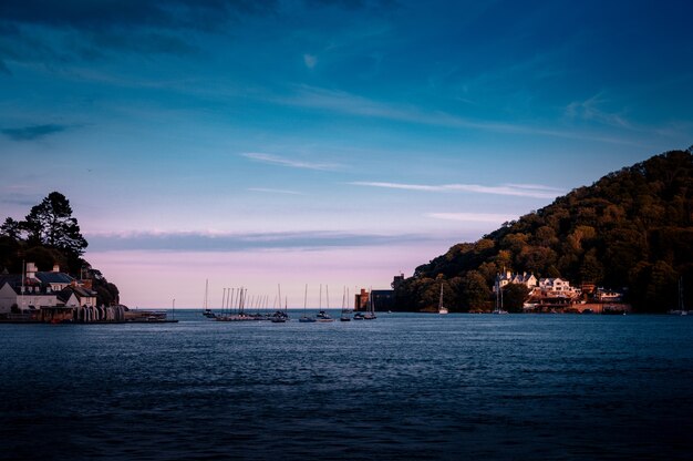 Een zee met schepen en gebouwen aan de kust, omgeven door hoge groene bergen in Dartmouth, UK