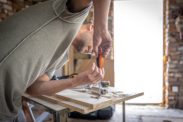 Een zelftappende schroef in een metalen bevestigingsgat op een houten strip schroeven met een schroevendraaier, het werk van een timmerman.