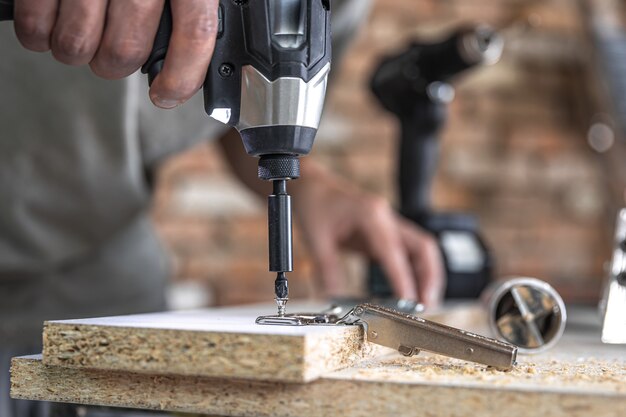 Een zelftappende schroef in een metalen bevestigingsgat op een houten strip schroeven met een schroevendraaier, het werk van een timmerman.