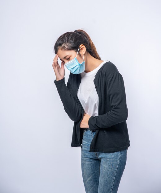 Een zieke vrouw met hoofdpijn droeg een masker en legde een hand op haar hoofd.