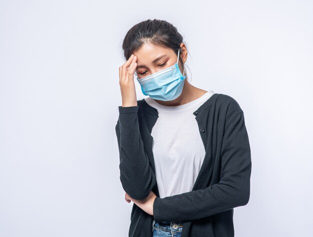 Een zieke vrouw met hoofdpijn droeg een masker en legde een hand op haar hoofd.