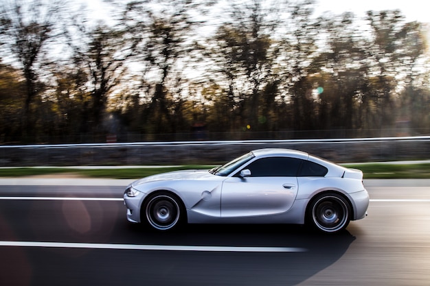 Een zilveren metallic kleurencoupé die door het bos rijdt.