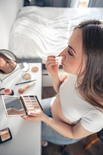 Een zwangere vrouw brengt thuis make-up aan voor een spiegel